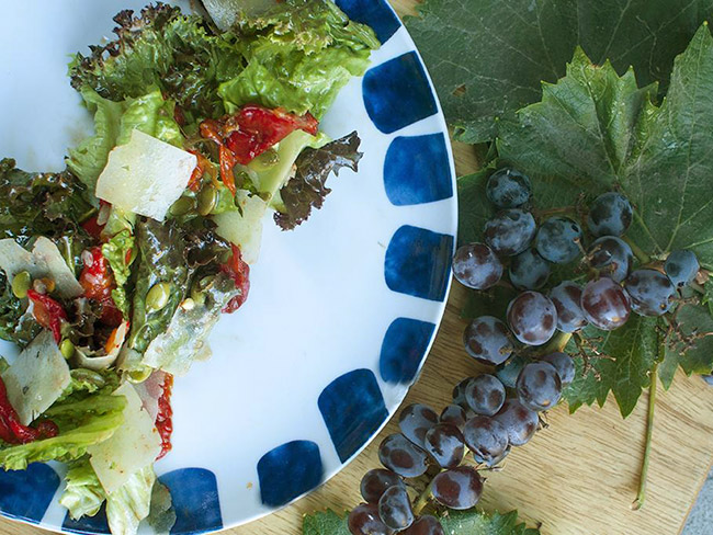 沙拉在白色和蓝色盘子上排列在一堆紫色的葡萄旁。