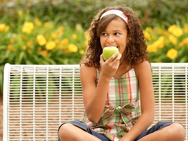 一个微笑的十几岁的女孩咬着一个绿色的苹果。