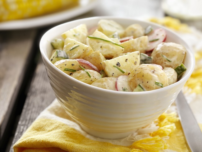 奶油土豆沙拉在木桌上的黄色餐巾纸上的白色碗中的奶油土豆沙拉。