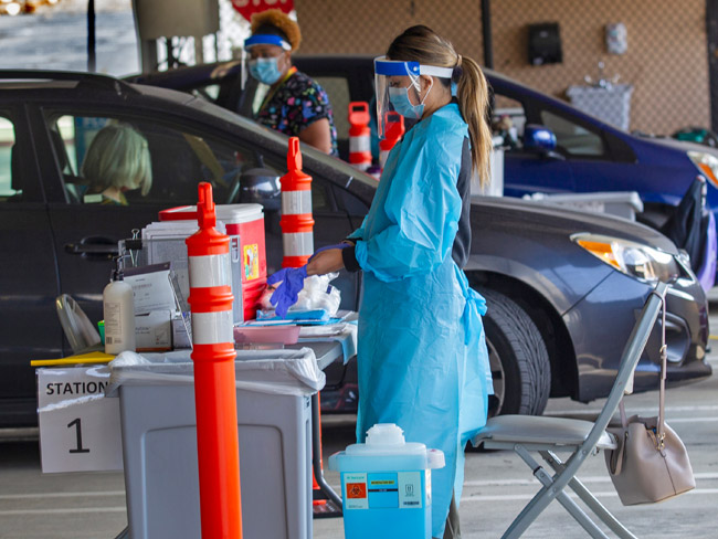 身着工作服的医护人员站在排队接受新冠病毒汽车检测的汽车前