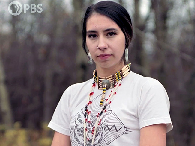一位年轻的美国土著妇女站在户外，戴着美国土著珠宝
