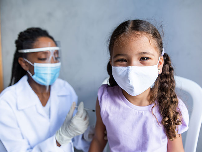 一个戴着口罩的小女孩在接种疫苗时微笑。
