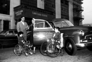 1952年，一辆车站旅行车的图像，一个男人和一个女人站在汽车旁边，有两个孩子坐在轮椅上。