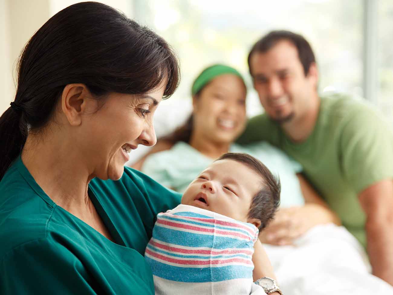 拿着有微笑的父母的护士拿着一个新出生的婴孩在背景中