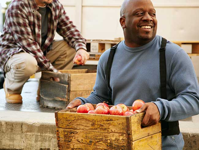 一个微笑的黑人拿着一箱苹果。