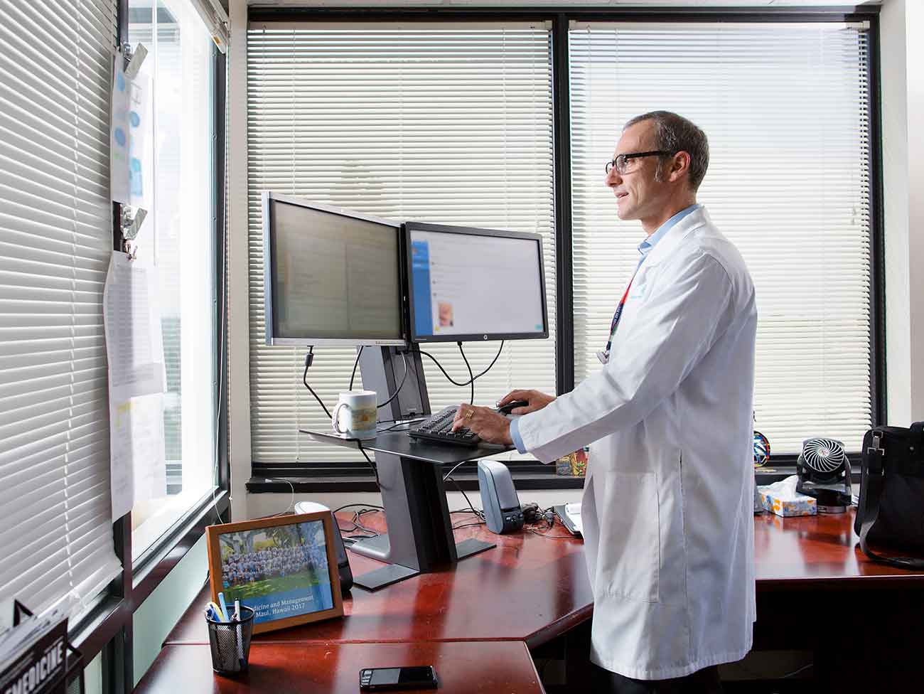 一名身穿白色博士服的男子站在一台带有双显示器的电脑前