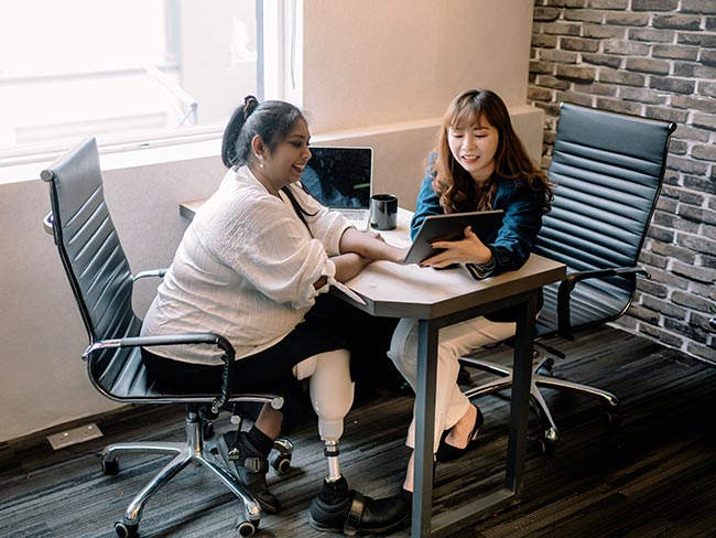 一位戴着假肢的女士在办公室工作台上和她的女同事讨论。