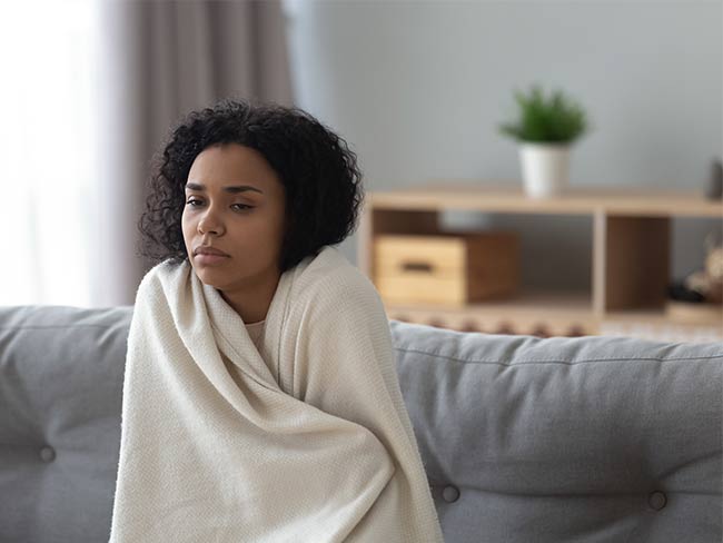 一个生病的女人裹着毯子，坐在沙发上。