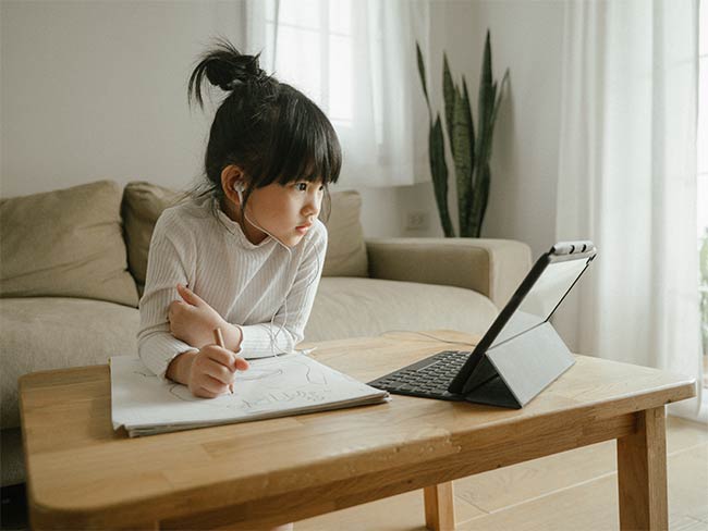 小女孩戴着耳机，在家里的客厅里使用数字平板电脑和电话会议应用程序学习