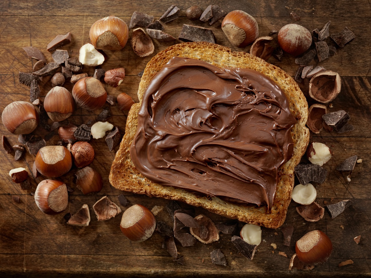 巧克力榛子蔓延在一块面包上，周围环绕着榛子