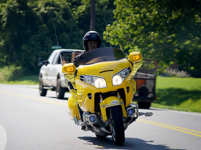 一个男人骑着一辆黄色的摩托车在路上。