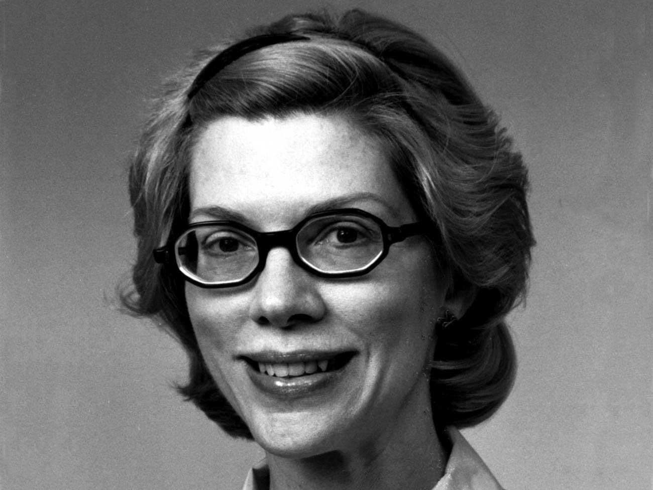 黑白照片，一个女人微笑着，戴着眼镜