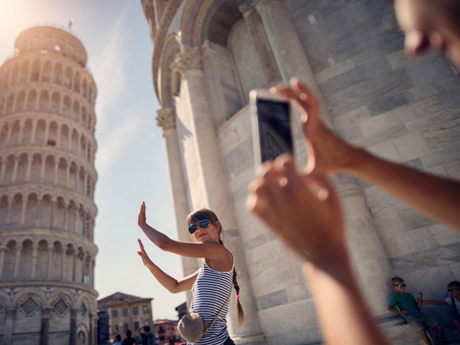 青少年在背景中与比萨的倾斜塔拍照