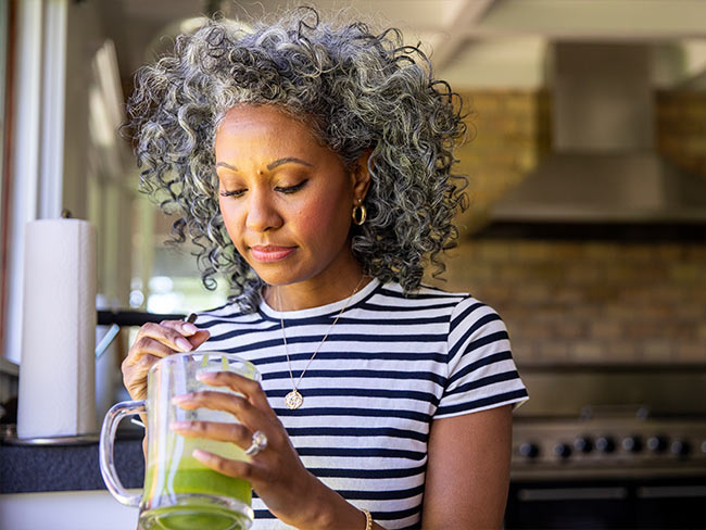 黑人妇女搅拌一杯绿色果汁。＂>
            </div>
            <div class=