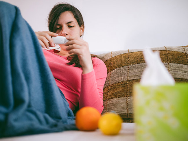 感冒或流感的女性躺在沙发上，检查体温
