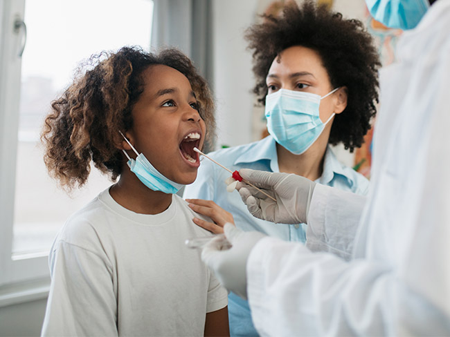 年轻的黑人女孩被她的母亲带到一家医疗诊所进行冠状病毒检测，正在进行口腔拭子测试。
