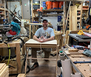 男人微笑着坐在车间工具和木材包围