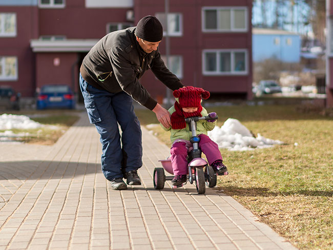 在一个寒冷而晴朗的冬日，爷爷教他蹒跚学步的孙女如何骑三轮车。