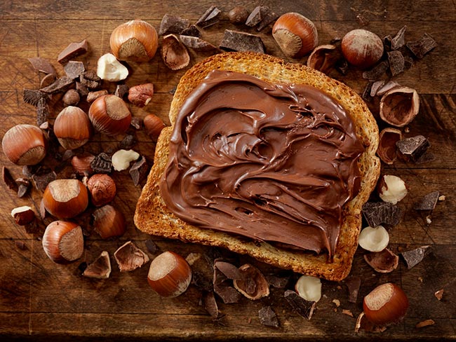 榛子巧克力铺在一片面包上，周围环绕着榛子