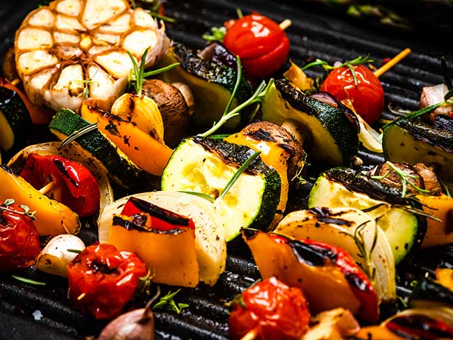 一个燃烧的烧烤架，上面有新鲜的夏季蔬菜串。