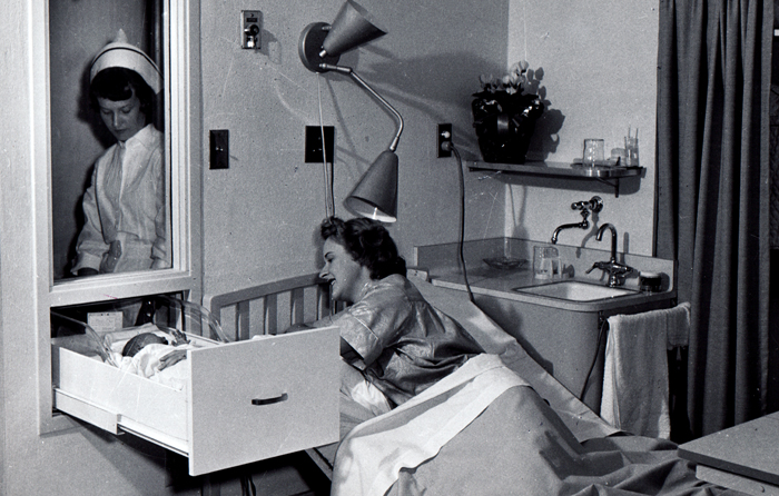 妇女躺在床上照顾挂在壁挂式滑动抽屉里的婴儿，凯撒基金会医疗中心护士看着