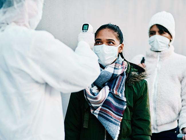 一名穿着PPE的卫生保健工作者正在用红外体温计测量一名年轻女子的体温。