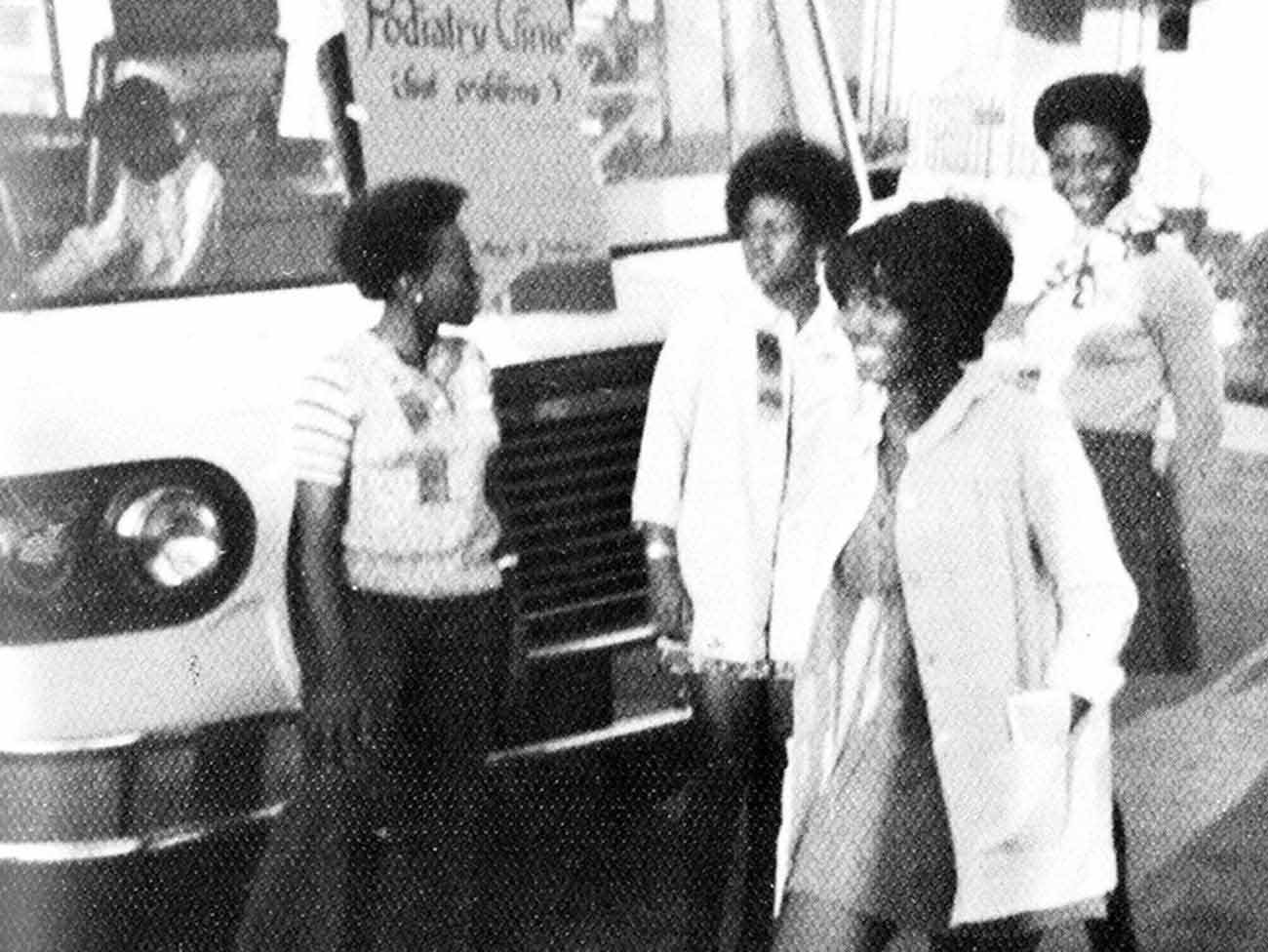 4名70年代的年轻女护理学生站在一辆大型移动医疗车前，车上的牌子上写着“足病诊所”。