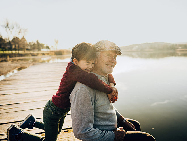 grandson hugging grandfather by a lake