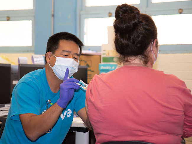 注册护士Sean Masaki在瓦胡岛的Aina Haina小学为一名家长接种疫苗。