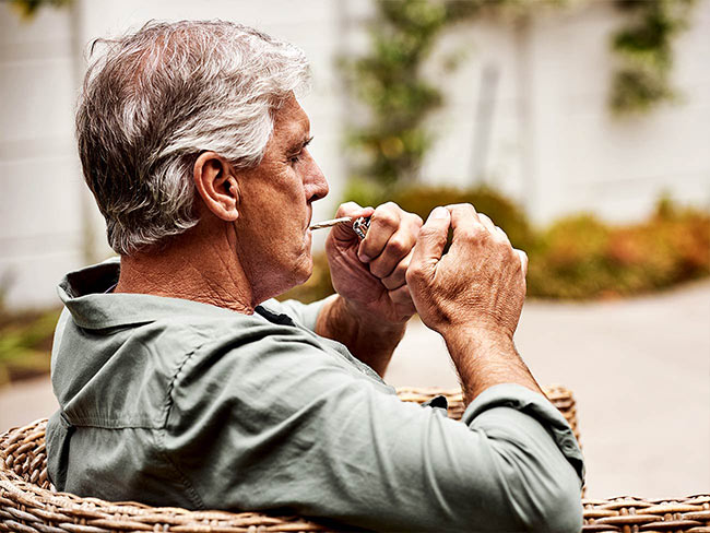 一个放松的老男人白天在家里的花园里自己抽大麻。