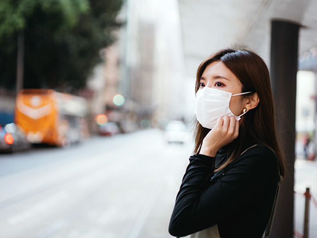 年轻的亚洲妇女戴着防护口罩等待公共交通工具。