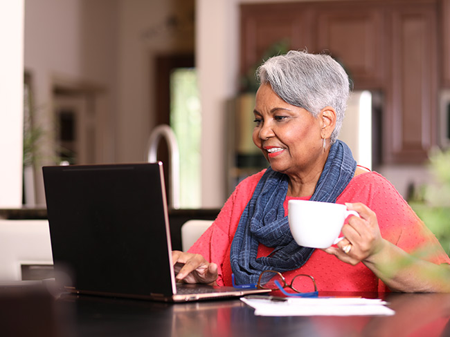 高级成年妇女在家里坐在厨房桌子上使用笔记本电脑。